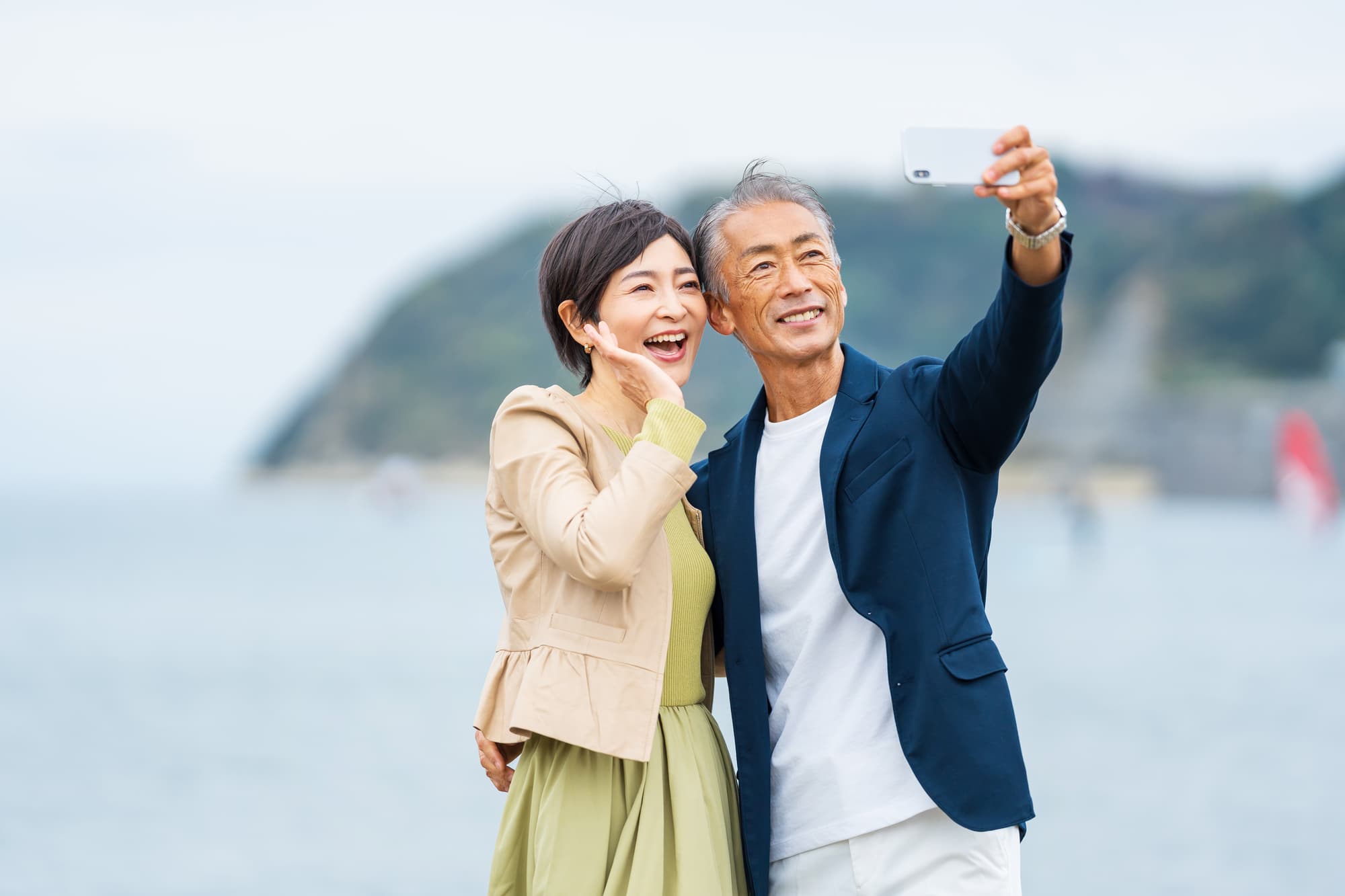 海をバックに二人で近づいて自撮りする夫婦