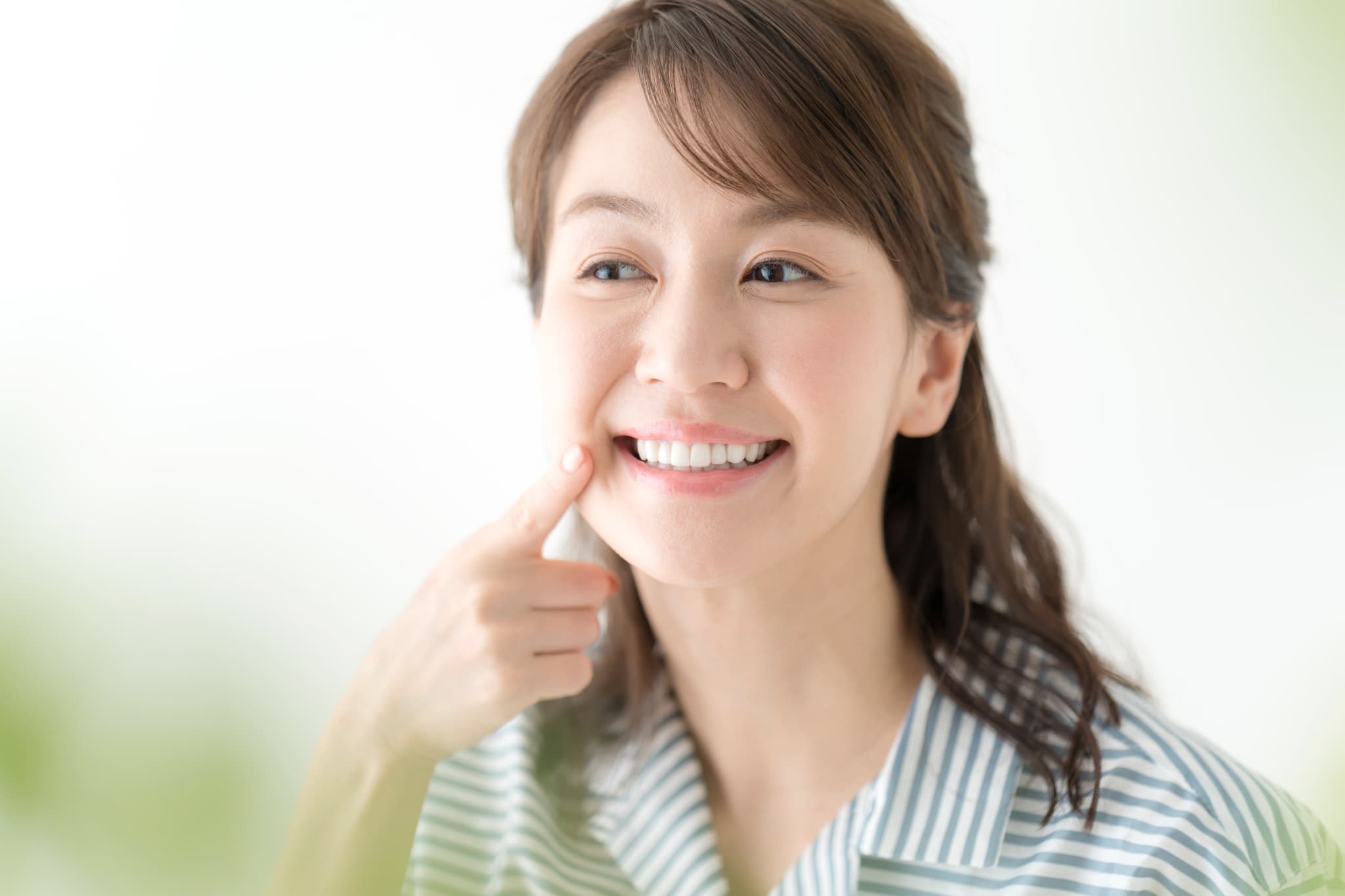 インプラントの歯を指さして笑顔を見せる女性